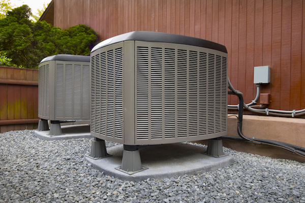 Outdoor heating and cooling system on stand above yard of rocks. Plugged into the side of a house.