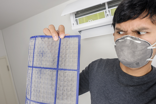 Man in face mask holding dirty air filter and looking at it with disgust