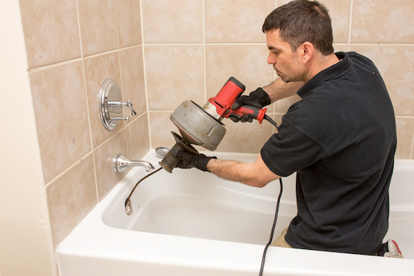 Plumber using auger on bathtub