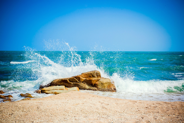 Waves breaking on a brown rock near a shoreline on a bright day. Water hammer.