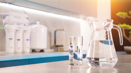 A pitcher of clean water in front of a reverse osmosis water filtration system.